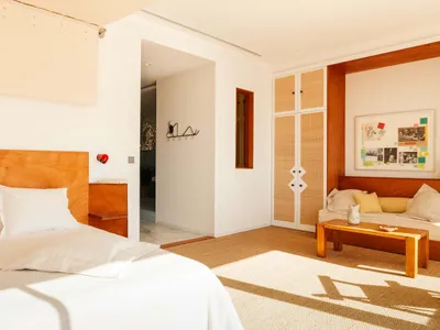 A modern minimalist bedroom featuring wooden furniture and woven fiber accents, with a bed, sofa, and coffee table.