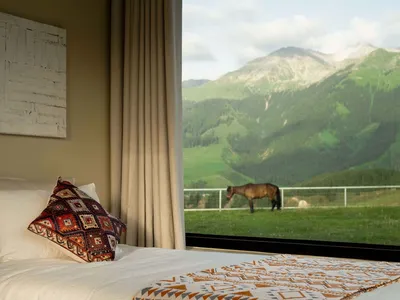 A bedroom with a bed featuring a bedspread and a pillow with a colorful geometric pattern, overlooking a mountain scene with
