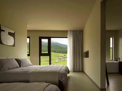 A modern minimalist bedroom featuring neutral-toned decor, a cozy bed, and a floor-to-ceiling window overlooking a green land
