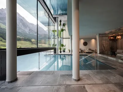 Modern pool lounge area with glass walls, concrete floor, and cushions.
