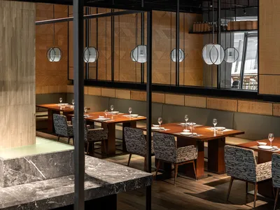 A modern restaurant interior with wooden tables, metal chairs, and glass elements.