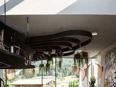 A modern restaurant interior featuring wooden tables, metal chairs, and hanging plants.