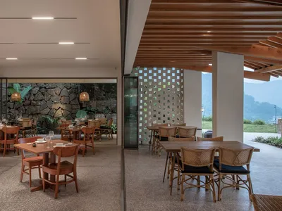 Modern restaurant interior with wood tables, stone walls, and glass accents.