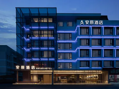 現代酒店外觀，搭配金屬框架、玻璃立面，以及暮色中的藍色燈光。