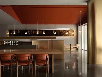 A modern restaurant interior with a terracotta ceiling and a gold pillar, showcasing contemporary design elements.
