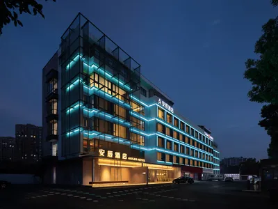 A modern hotel exterior featuring glass walls and illuminated by LED lighting at dusk.