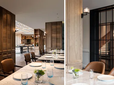 Modern restaurant interior with marble walls, wooden panels, leather chairs, and a steel and glass door.