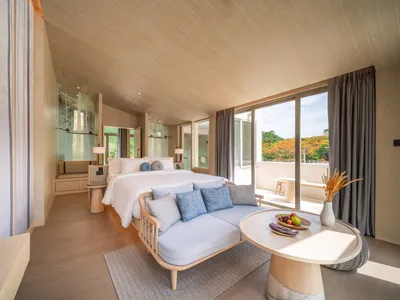 Modern minimalist bedroom featuring a white bed with blue pillows, a wooden sofa, a round table with a fruit plate, and a lar