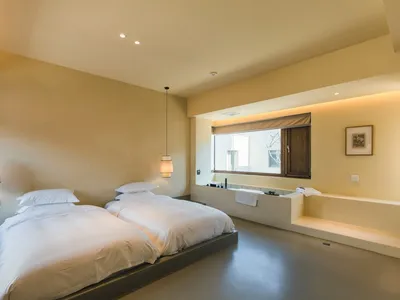 A minimalist bedroom with neutral tones features twin beds, pendant lamps, and a window.