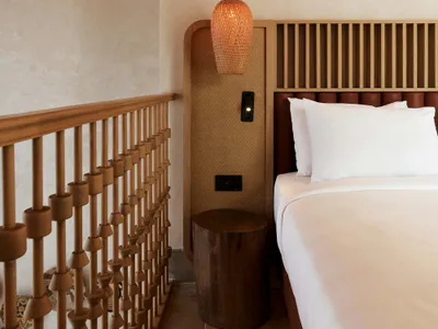 Minimalist bedroom featuring a wooden bed with a wooden headboard and a wooden bedside table with a woven pendant lamp.