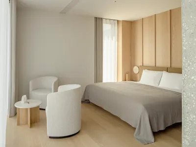 A minimalist bedroom with a circular desk chair, a circular side table, and a bed with a white shade.