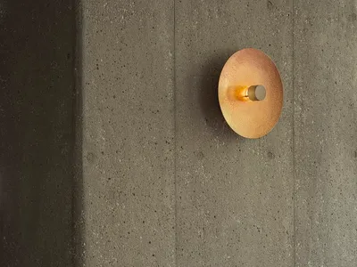 Minimalist restaurant interior featuring a concrete wall, wooden chair, and round gold light fixture.