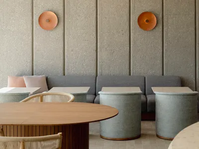 Modern restaurant interior with concrete walls, fabric seating, and wooden tables and stools.