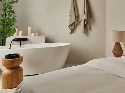 A minimalist bedroom with neutral materials and a white freestanding bathtub.