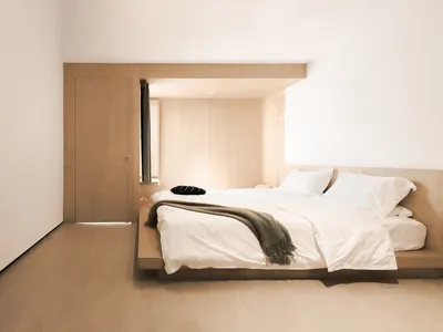 A minimalist bedroom with a floating bed platform, wooden walls, and a simple arrangement of pillows and a blanket.
