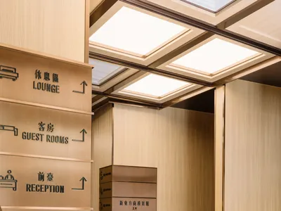 現代酒店室內，木質天花板、瓷磚地板，以及標示休息室、客房、接待處與電梯的指示牌。
