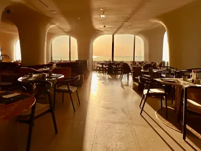 A spacious modern restaurant features stone-floored dining areas with minimalist decor and large windows.