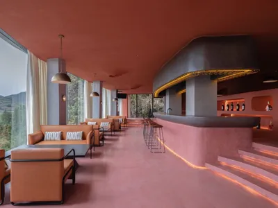 Modern minimalist restaurant bar with concrete walls and seating, large windows overlooking the landscape.