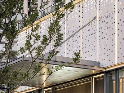Modern hotel exterior featuring metal and glass materials, surrounded by green landscaping.