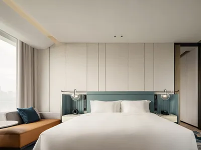 Modern minimalist bedroom with white bed, blue-green headboard, and white sheets.