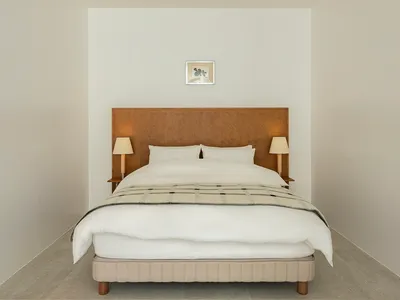 A minimalist bedroom featuring a neutral-toned bed with a simple headboard, side tables with lamps, and a framed picture on t