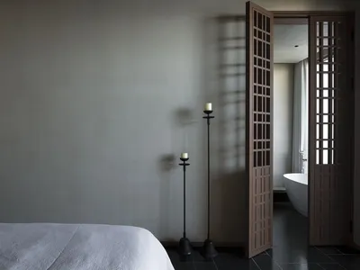 簡約臥室內擺放白色床鋪、燭台，背景可見浴缸，展現現代寧靜氛圍