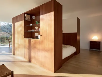 Modern minimalist bedroom with wooden cabinets, glass shelves, and a bed.