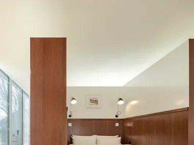 A minimalist bedroom with a wooden bed platform and paneling, featuring a cozy white bed and ambient lighting.