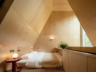 Modern minimalist bedroom with wooden walls, floor, and furniture, featuring a comfortable bed with white bedding and a singl