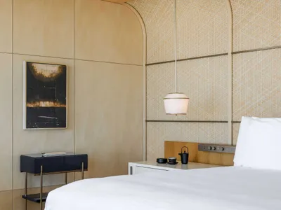 A minimalist bedroom with a white bed, wood wall panels, and a hanging lamp.
