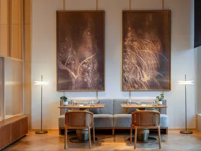 A minimalist restaurant interior with two tables, chairs, and large abstract paintings on the wall