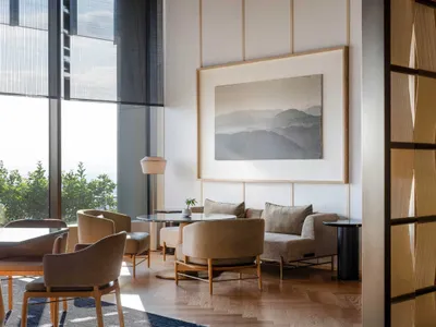 Sunny modern lounge area featuring minimalist furniture, neutral colors, and a large window view of distant mountains.