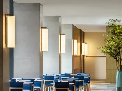 Modern restaurant interior featuring concrete pillars, wooden furniture, and blue chairs.