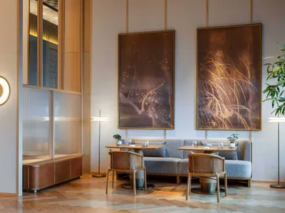 A modern restaurant interior with wooden furniture, featuring a seating area with tables, chairs, and large artwork on the wa