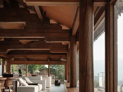 A spacious, industrial-style living room with exposed wooden beams and a large window overlooking a serene landscape.