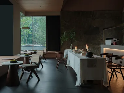 A modern restaurant dining room featuring stone flooring, sleek furniture, and natural light.