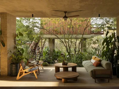 A cozy industrial living room with a wooden sofa, wood and concrete tables, and a concrete ceiling and pillars.