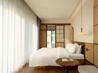 A minimalist bedroom featuring a white bed, wooden flooring, and a modern hanging lamp.