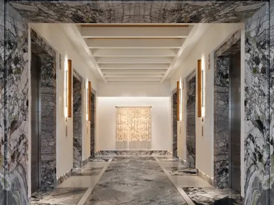 一條長而優雅的走廊，鋪設大理石地板與牆面，盡頭擺放獨特的玻璃藝術裝置。