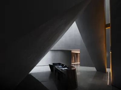 A minimalist hotel reception area with concrete walls and a sleek, black reception desk.