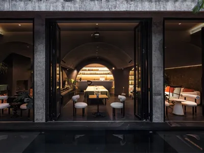 Industrial-themed restaurant lounge with concrete walls, glass dining area, and modern decor.