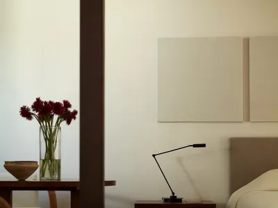 Modern, minimalist bedroom with wooden furniture and a vase of red flowers on a table.
