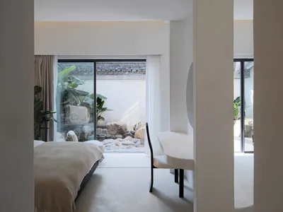 A minimalist bedroom features concrete and glass materials with soft furnishings and a serene space.