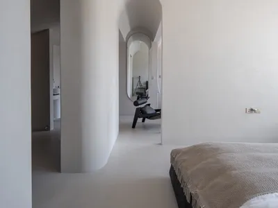 A modern minimalist bedroom featuring a concrete floor and walls with a low-profile bed and black chair.
