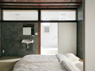 A minimalist bedroom with a concrete wall and floor, featuring a white bed and sink.