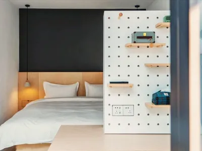 Modern minimalist bedroom with a bed featuring white bedding and a white wooden headboard, illuminated with warm lighting fro