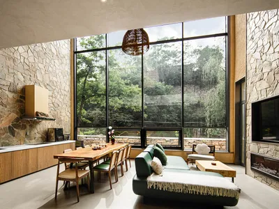 A modern industrial living room with a wooden table and green sofa overlooking a forest.