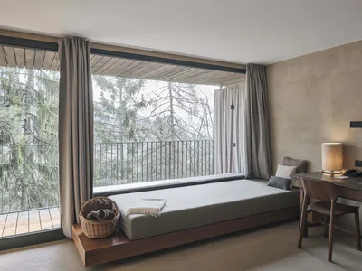 Modern bedroom with a floating bench, wooden beams, and a view of the forest through large windows.