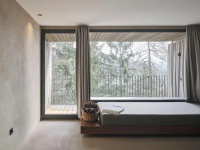 A modern bedroom featuring a hanging platform with wood and plaster finishes, overlooking a scenic tree-filled balcony.