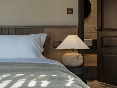 A minimalist bedroom with a comfortable bed, a table lamp, and a door leading to an attached bathroom.